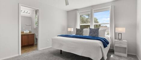 Une chambre à coucher avec un lit, un ventilateur de plafond, une fenêtre avec des rideaux et une table de chevet avec une lampe.