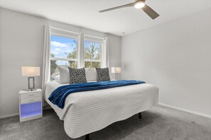 Quarto com cama, mesas de cabeceira, ventilador de teto e janela com cortinas.