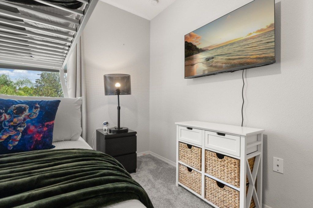 Een slaapkamer met een bed, nachtkastje, lamp, televisie en opbergmanden.