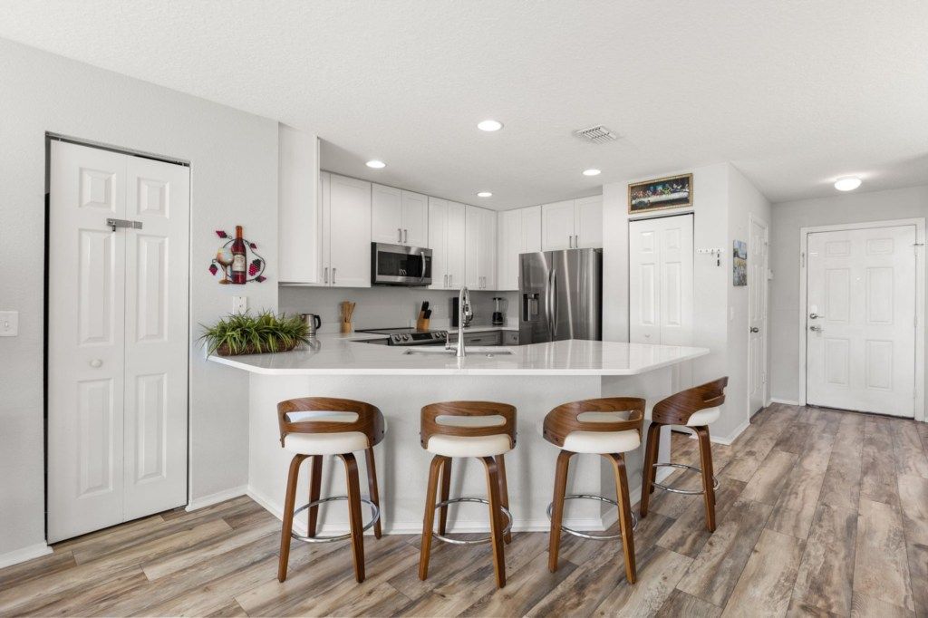 A modern kitchen with white cabinetry, stainless steel appliances, and a central island with bar stools.