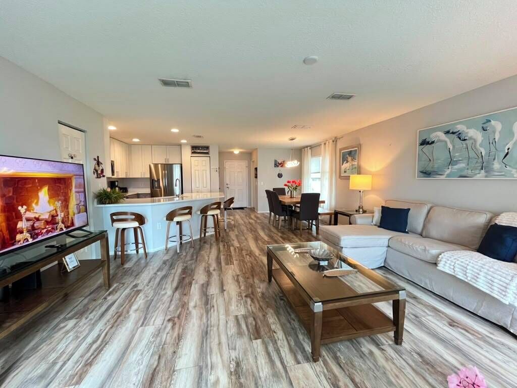 A modern living room with a flat-screen TV, a glass coffee table, a sofa, and a dining area with chairs and a table.
