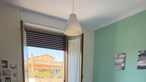 Ett sovrum med en säng, ett fönster med persienner, en hängande lampa och konstverk på väggen.