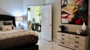 Ein Schlafzimmer mit Bett, Nachttisch, Schminktisch und einem großen abstrakten Gemälde.