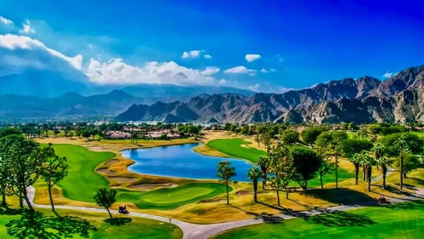 Ein Golfplatz mit einem See, Bäumen und Bergen im Hintergrund.