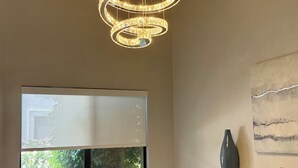 Ein moderner Essbereich mit einem großen Tisch, Stühlen, einer dekorativen Chandelier und einem Fenster mit Blick auf Grünflächen.