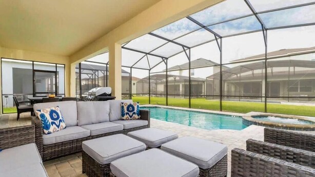 Un espace extérieur abrité avec une piscine, des meubles en osier et une vue sur le jardin arrière.