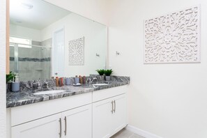 Une salle de bain dotée d’un comptoir en marbre, de deux lavabos, d’un grand miroir et d’œuvres d’art décoratives murales.