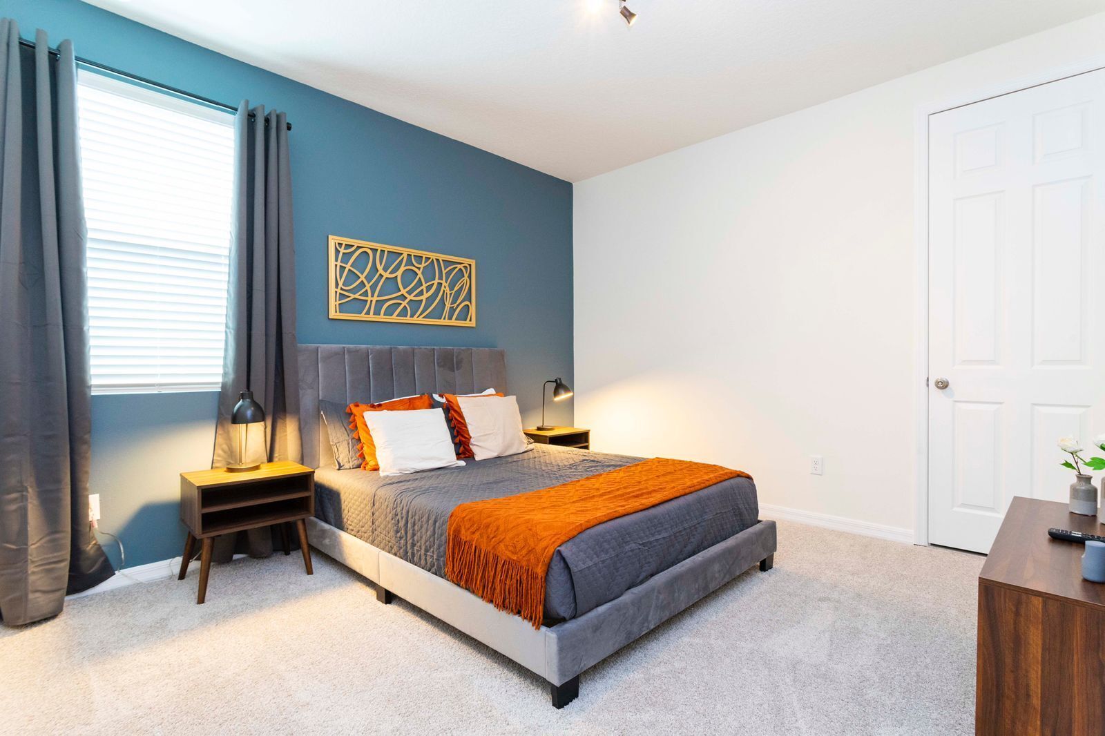 A bedroom with a bed, nightstands, a lamp, a decorative wall piece, and a door.