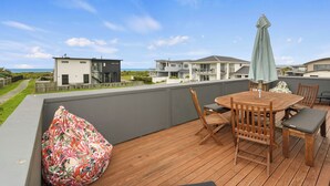 Um deck de madeira com mesa e cadeiras, um guarda-sol verde e um bean bag colorido.