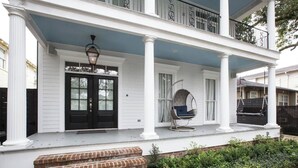 Een woonhuis met twee verdiepingen, een veranda, een voordeur en een schommelstoel.