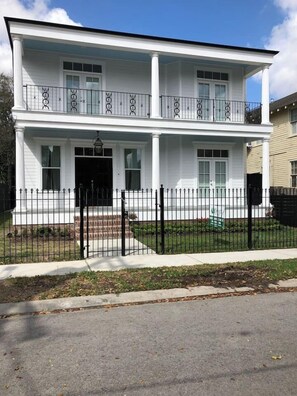 A two-story house with a front porch, a black metal fence, and a clear sky. - Maison de l'Artiste | Curated NOLA Stay, Near the FQ (New Orleans)