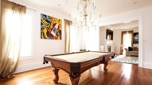 Een ruime kamer met een pooltafel, een kroonluchter en een schilderij aan de muur.
