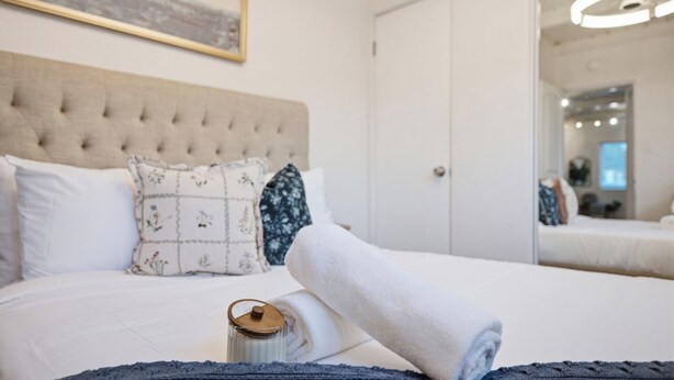 Un lit bien fait, avec une serviette blanche roulée, un coussin décoratif et un récipient en verre posé sur le lit.