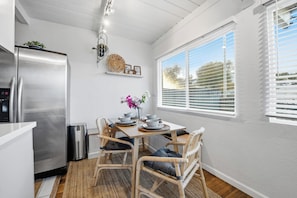 A compact kitchen with a stainless steel refrigerator, a dining table with chairs, and a window with blinds. - Stylish 2BR Home | Parking & AC | Near Downtown (San Diego)