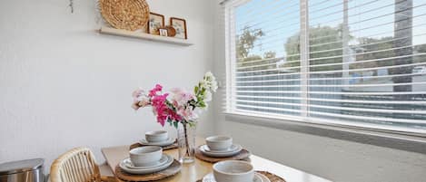 A dining area with a wooden table set for four, white plates, and a vase with pink flowers.