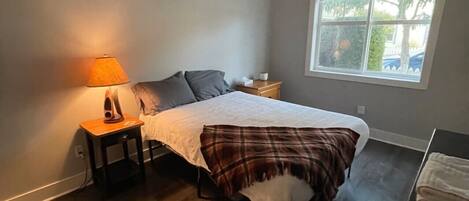A bedroom with a bed, a nightstand, a lamp, a window, and a ceiling light.