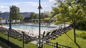 Piscina con sillones de descanso, una valla y montañas al fondo.