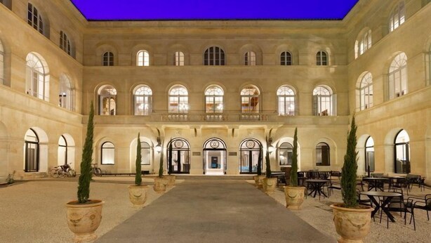 A spacious courtyard with a central open area, surrounded by columns and arches, and potted plants along the perimeter.