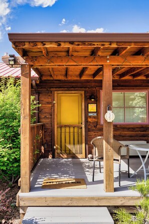 Eine Holzhütte mit Veranda, einer gelben Tür, einem 'SUNRISE'-Schild, einem Korbstuhl und einer Fußmatte mit der Aufschrift 'WELCOME'.
