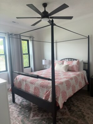 Ein Bett mit Baldachin, ein Deckenventilator, ein Fenster mit Vorhängen und ein gemustertes Teppich.