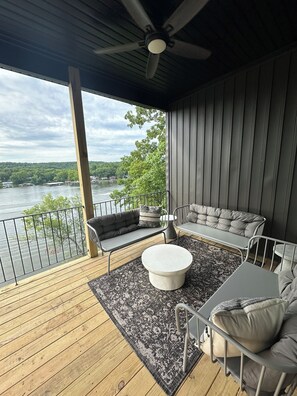Eine überdachte Terrasse mit Seeblick, einer Couch, einem Tisch und einem Deckenventilator.