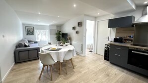 Una cocina moderna con un extractor de aire negro, un comedor con una mesa redonda y sillas, y un sofá gris al fondo.