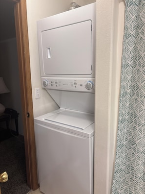A compact, white front-loading washer and dryer unit with a control panel featuring various settings. - Spacious 2-Bedroom. Attached Garage, Fenced Yard & Patio, Close to Everything (Moses Lake)