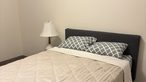 Uma cama com cobertura acolchoada, luminária de cabeceira e travesseiro estampado.