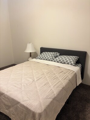 A bed with a quilted cover, a bedside lamp, and a patterned pillow. - Spacious 2-Bedroom. Attached Garage, Fenced Yard & Patio, Close to Everything (Moses Lake)