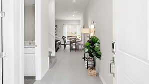 En hall som leder till ett matområde med ett bord och stolar, en växt och en lampa.