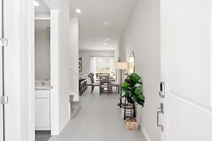 Ein Flur, der in einen Essbereich mit Tisch und Stühlen, einer Pflanze und einer Lampe führt.