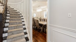 Eine Treppe mit dunkler Geländer und Teppichstufen führt zu einem Essbereich mit Holzboden und einer Deckenleuchte.