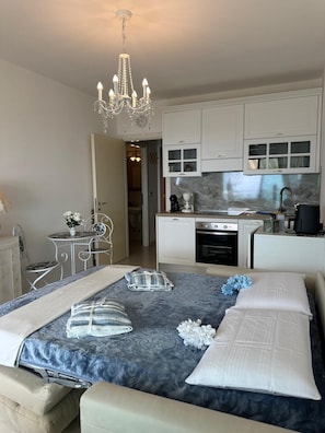 Ein Schlafzimmer mit einem Bett, Nachttischen, einer Chandelieber, einer Essecke mit Tisch und Stühlen sowie einer Küche mit Schränken und Geräten.