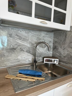 Eine Küche mit einem Edelstahl-Spülbecken, einer Marmor-Spritzschutzwand und einem Schrank mit Glastür.