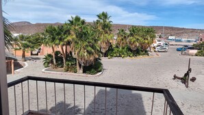 A paved area with palm trees, a metal railing, and parked cars. - Playa Condo 7 P.Alta cerca Balandra (La Paz)