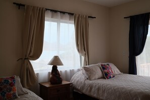 Une chambre avec deux lits, une table de chevet, une lampe et une fenêtre avec des rideaux.