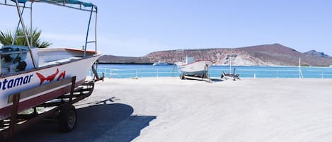 Un bateau nommé « Tamar » est posé sur une remorque, un deuxième bateau se trouve sur la plage, et un ciel bleu dégagé surplombe un paysage vallonné.