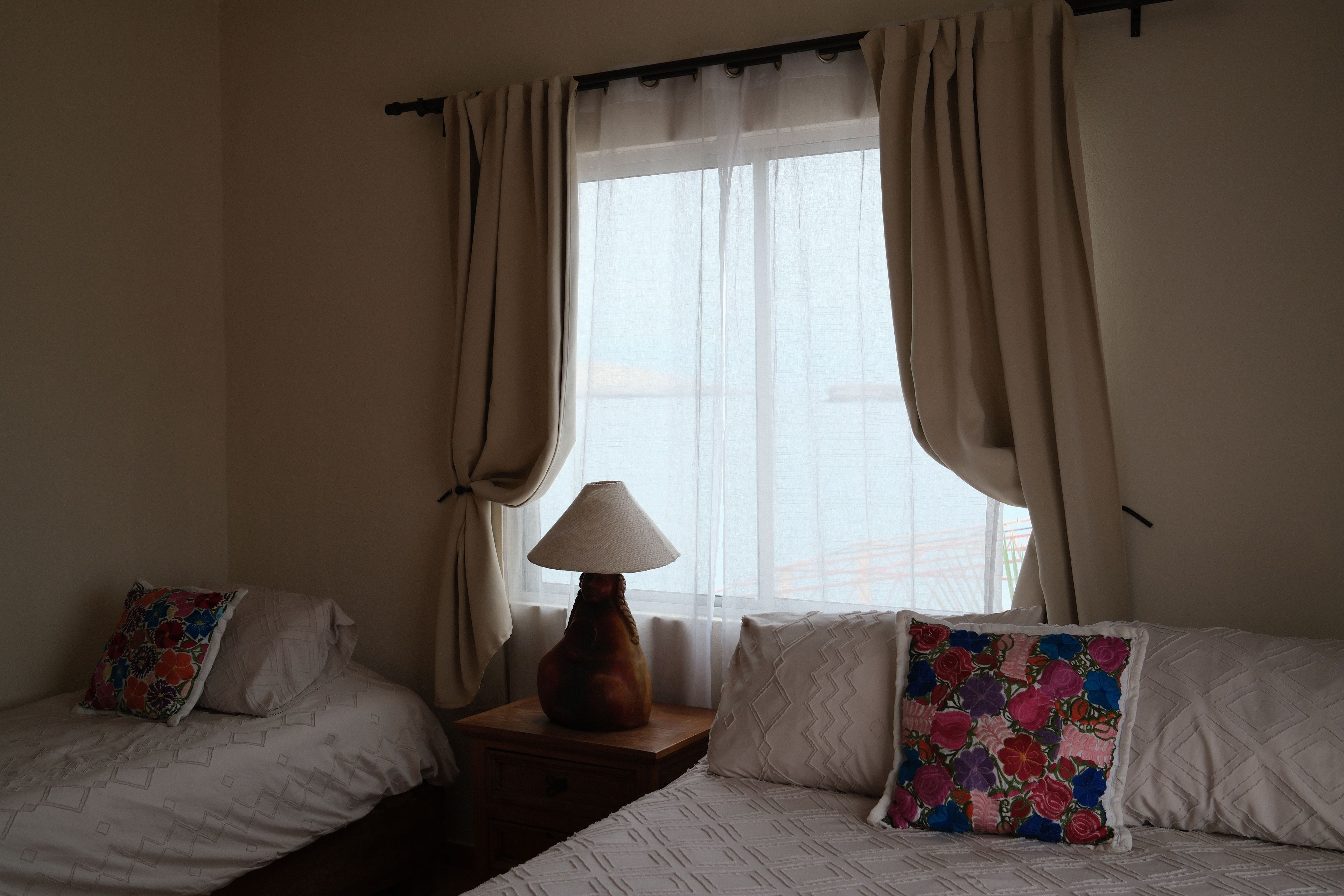 Ein Hotelzimmer mit zwei Betten, einem Nachttisch, einer Lampe und einem Fenster mit Vorhängen.