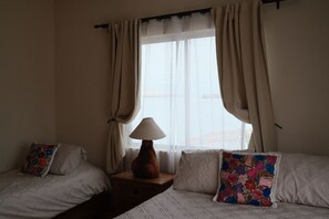 Een hotelkamer met twee bedden, een nachtkastje, een lamp en een raam met gordijnen.