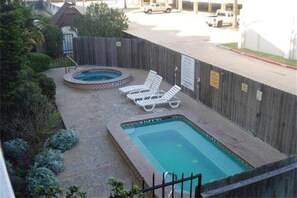 Ein rechteckiger Pool mit zwei Liegestühlen und einer Whirlpool, umgeben von einem Holzzaun.