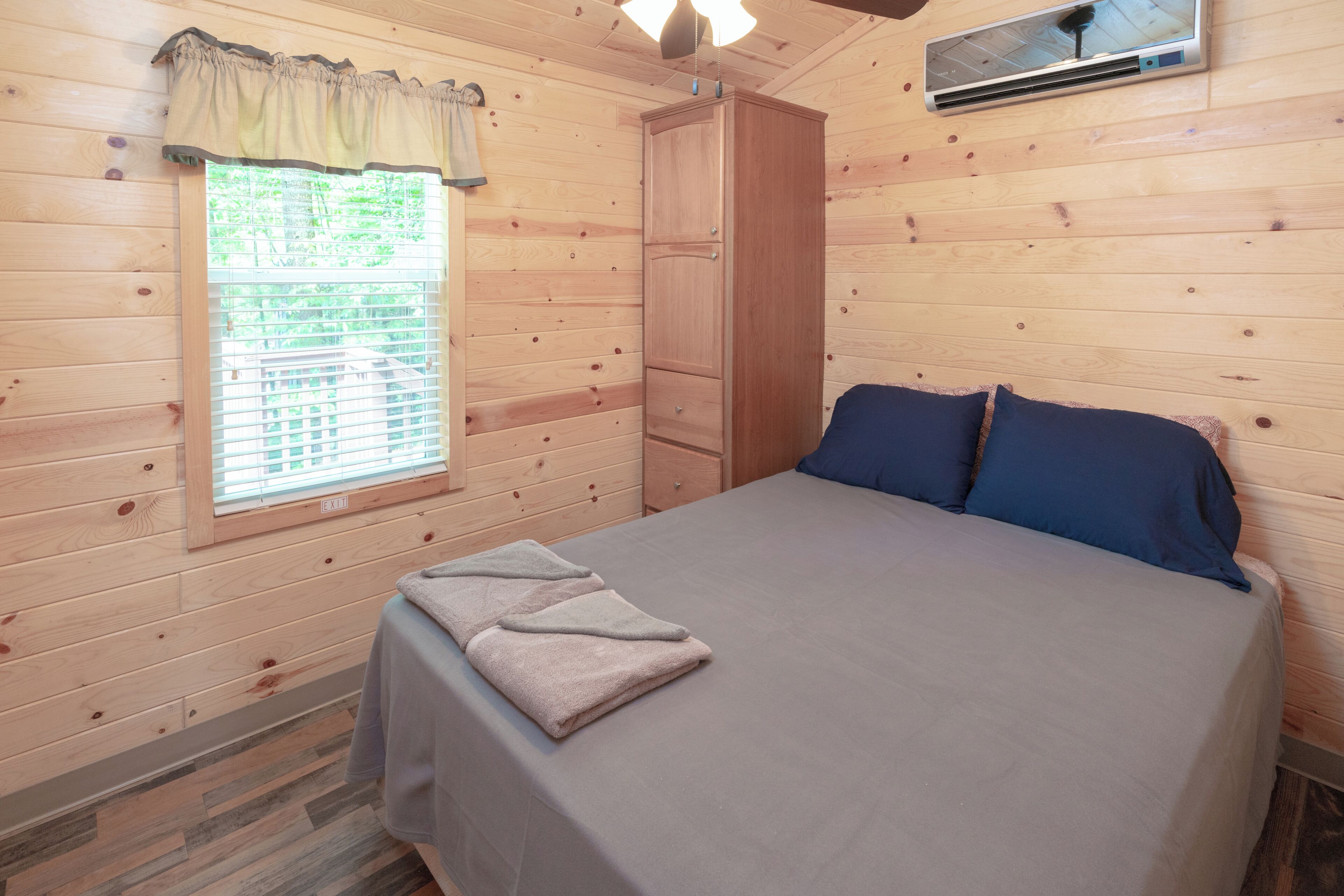Una habitación de cabaña de madera con cama, armario y ventana con persianas.