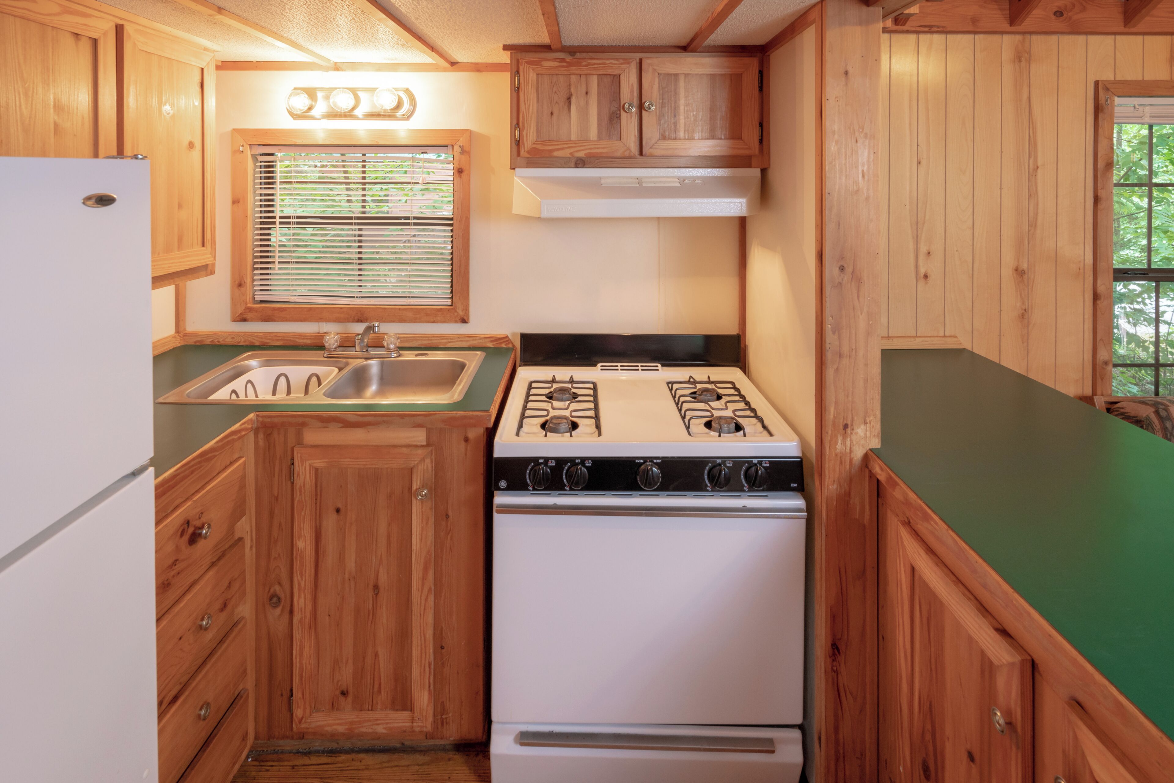 Une cuisine de taille réduite, dotée de meubles en bois, d’une cuisinière à gaz, d’un évier et d’un réfrigérateur.