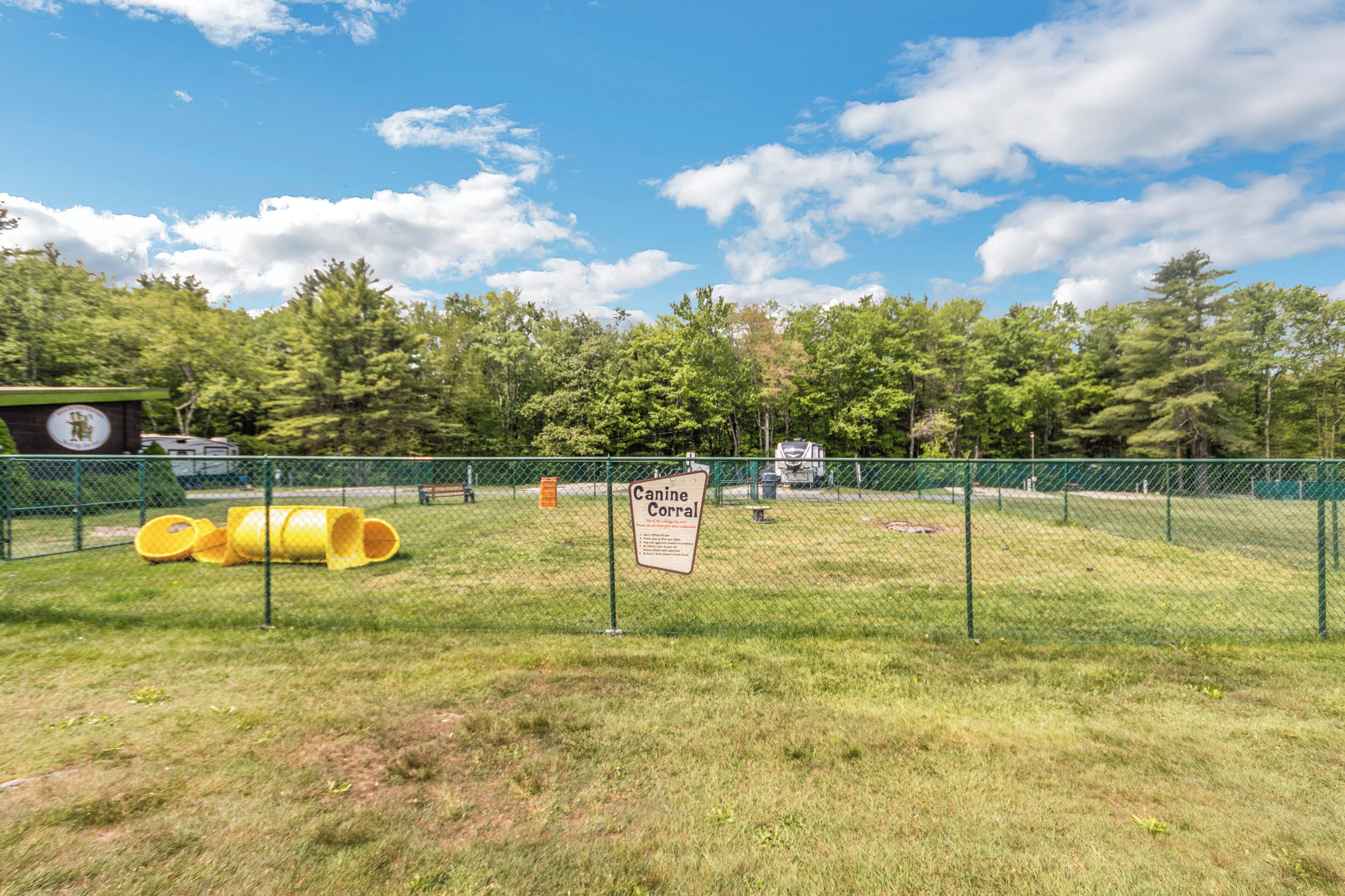 Un espace clos, aménagé en parc, avec une pancarte indiquant « Enclos canin » et une structure de jeux jaune.