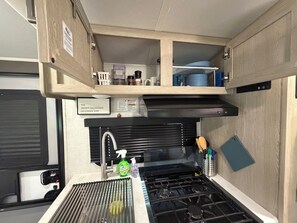 Een kleine keuken met een fornuis, spoelbak en houten kastjes.