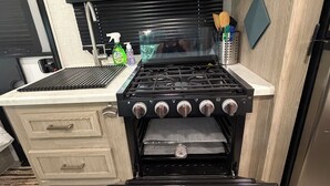 Una cucina compatta con fornello, forno e lavello. Asciugamani appesi alla porta del forno.