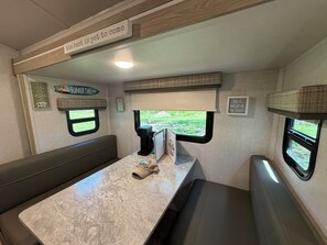 Ein kompaktes Wohnmobil-Interieur mit Essbereich, Kaffeemaschine und Fenster mit Blick auf Grünflächen.