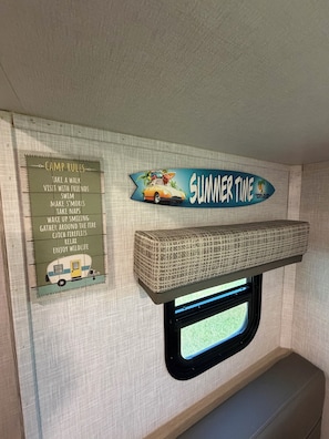 Ein Campervan-Innenraum mit einem an der Wand befestigten Schild, das sommerliche Aktivitäten auflistet, und einem Fenster mit Blick hinaus.