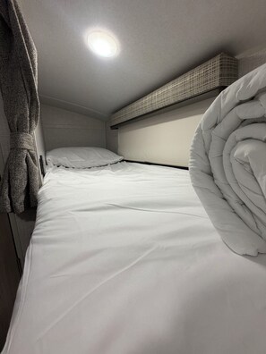 Een enkel bed met witte lakens, een hoofdeinde en een plafondlamp.