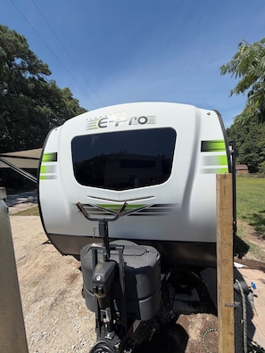 Ein weißer Wohnmobilwagen mit 'E-Pro'-Branding, einem nach vorne schwenkbaren Spülbecken und einem Holzpfosten in der Nähe.