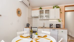Een moderne keuken met witte kasten, een magnetron, een koffiezetapparaat en een eethoek met een witte tafel en stoelen.